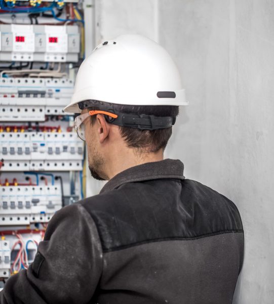 Man, an electrical technician working in a switchboard with fuses. Installation and connection of electrical equipment. Professional with tools in hand. concept of complex work, space for text.