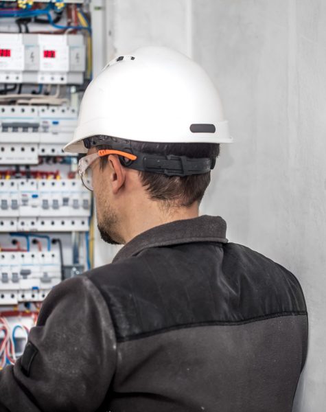 Man, an electrical technician working in a switchboard with fuses. Installation and connection of electrical equipment. Professional with tools in hand. concept of complex work, space for text.